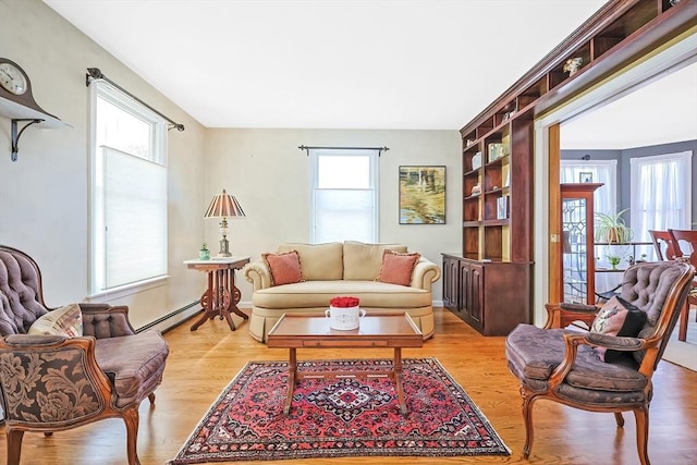 living area featuring baseboard heating, light wood-style floors, and a healthy amount of sunlight