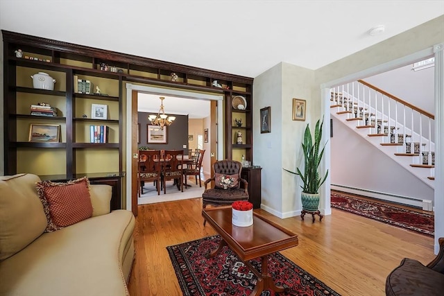 living area with wood finished floors, stairway, an inviting chandelier, a baseboard radiator, and baseboards