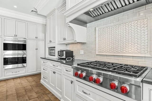 kitchen with visible vents, dark countertops, custom range hood, appliances with stainless steel finishes, and white cabinetry