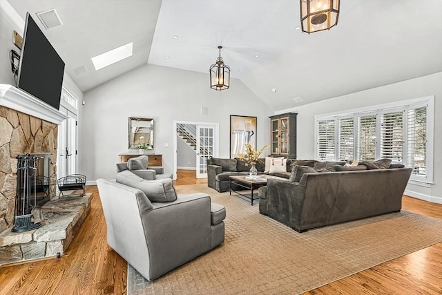 living room featuring a skylight, a fireplace, wood finished floors, high vaulted ceiling, and stairs