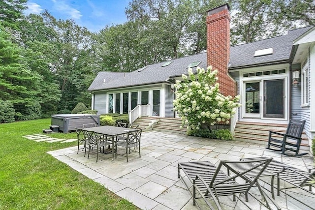 back of house with entry steps, a hot tub, a shingled roof, a chimney, and a patio area