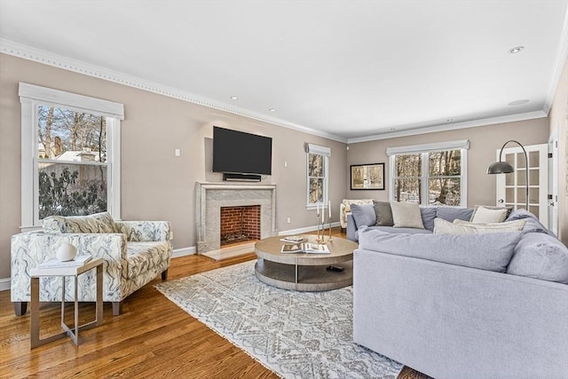 living room with crown molding, a premium fireplace, baseboards, and wood finished floors