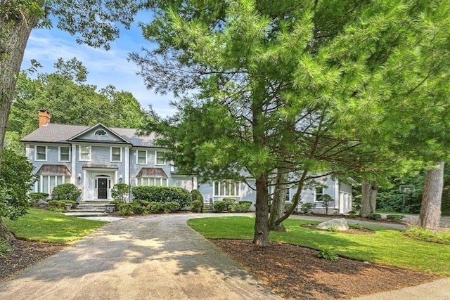 view of front of property featuring driveway, a chimney, and a front yard