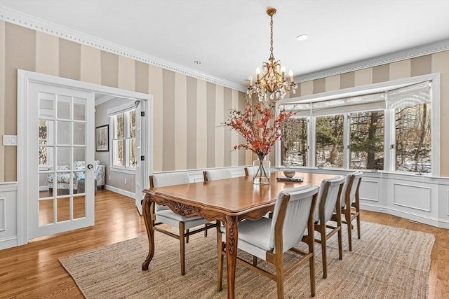 dining room featuring a decorative wall, ornamental molding, light wood-type flooring, wallpapered walls, and an inviting chandelier