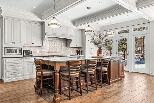 kitchen with an island with sink, tasteful backsplash, stainless steel microwave, and ornamental molding