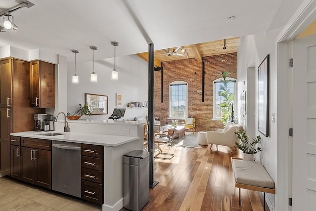 kitchen featuring brick wall, open floor plan, light countertops, a sink, and dishwasher