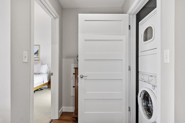 laundry area with laundry area, stacked washer and dryer, dark wood-style flooring, and baseboards
