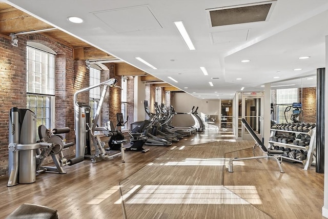 exercise room with brick wall, visible vents, and wood finished floors
