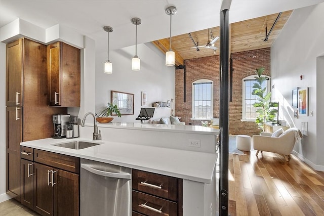 kitchen with stainless steel dishwasher, a peninsula, brick wall, open floor plan, and a sink