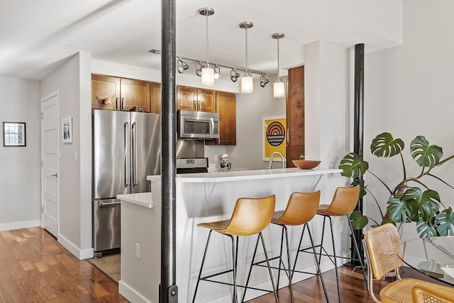 kitchen with hanging light fixtures, brown cabinets, wood finished floors, a breakfast bar, and stainless steel appliances