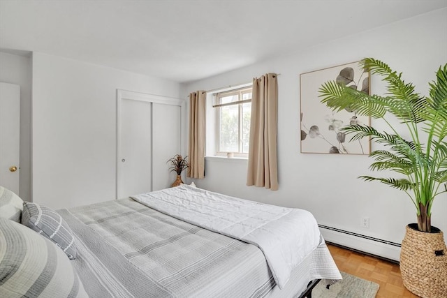 bedroom featuring baseboard heating, a closet, and light parquet floors