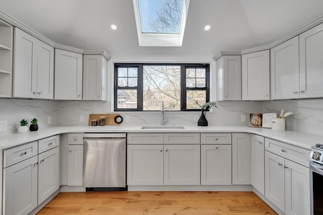 kitchen featuring vaulted ceiling with skylight, light hardwood / wood-style floors, decorative backsplash, sink, and stainless steel appliances