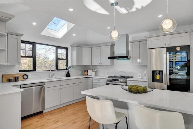 kitchen with pendant lighting, sink, a kitchen breakfast bar, stainless steel appliances, and wall chimney exhaust hood