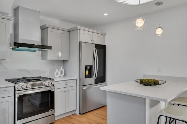 kitchen with a kitchen bar, decorative light fixtures, wall chimney range hood, stainless steel appliances, and tasteful backsplash