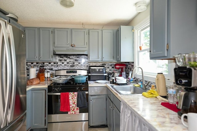 25 Sutherland St, Lowell, MA 01850 - kitchen featuring stainless steel appliances, under cabinet range hood, gray cabinetry, light countertops, and tasteful backsplash