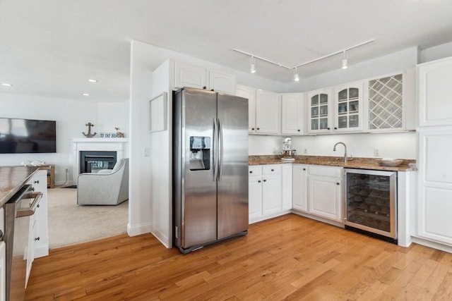 kitchen with appliances with stainless steel finishes, beverage cooler, glass insert cabinets, light wood-style floors, and recessed lighting