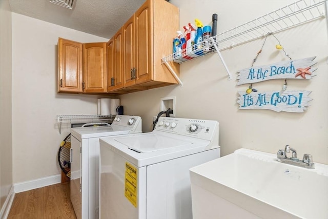 washroom with cabinet space, light wood-type flooring, washer and clothes dryer, and baseboards
