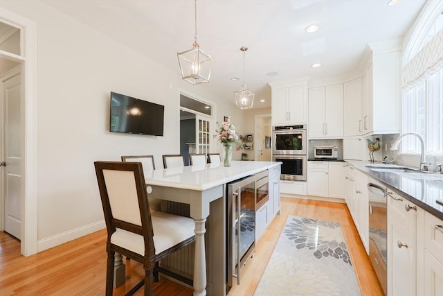 kitchen featuring appliances with stainless steel finishes, a sink, wine cooler, light wood-style floors, and white cabinetry