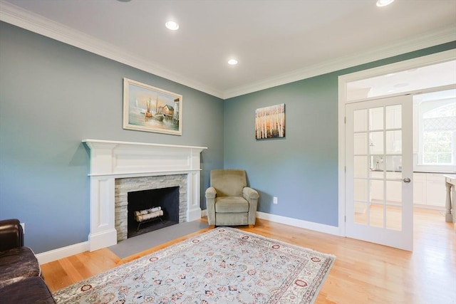 living area featuring light wood-type flooring, crown molding, a stone fireplace, recessed lighting, and baseboards