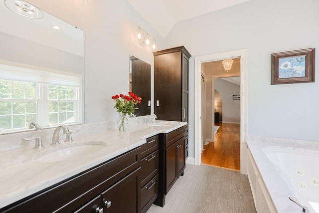 bathroom with double vanity, a tub with jets, and vaulted ceiling