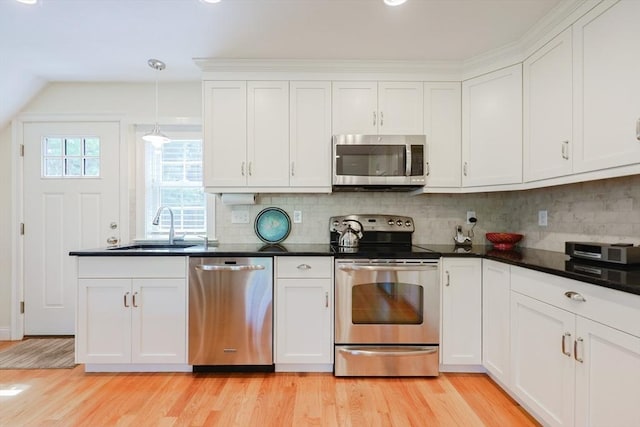 kitchen featuring appliances with stainless steel finishes, a sink, light wood-style flooring, white cabinetry, and dark countertops