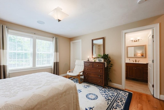 bedroom featuring baseboards, light wood finished floors, ensuite bathroom, and a sink