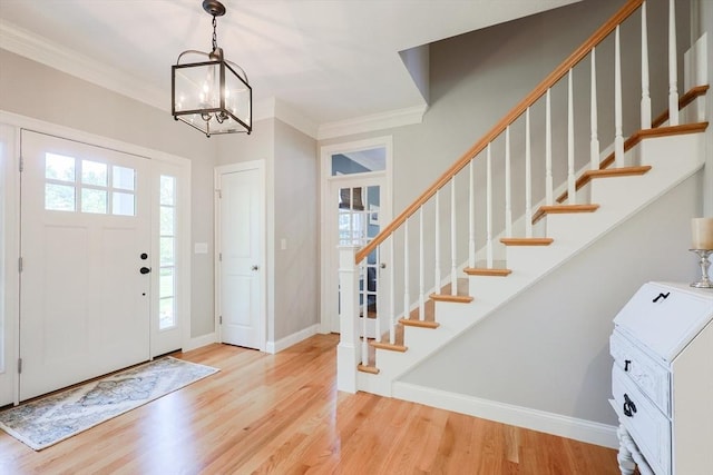 foyer entrance featuring wood finished floors, crown molding, stairs, a chandelier, and baseboards