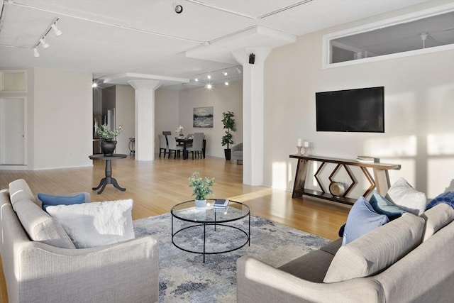 living room with decorative columns, rail lighting, and light hardwood / wood-style flooring