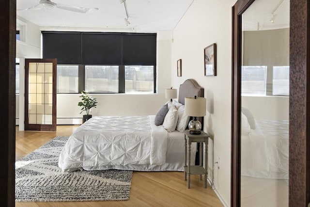 bedroom featuring a baseboard heating unit, ceiling fan, track lighting, and light wood-type flooring