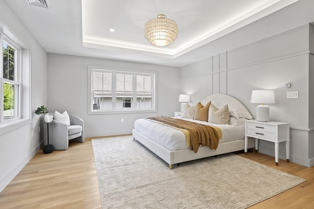 bedroom featuring a raised ceiling and light hardwood / wood-style flooring