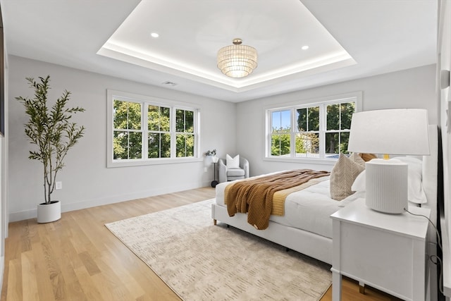 bedroom with light wood-type flooring and a raised ceiling