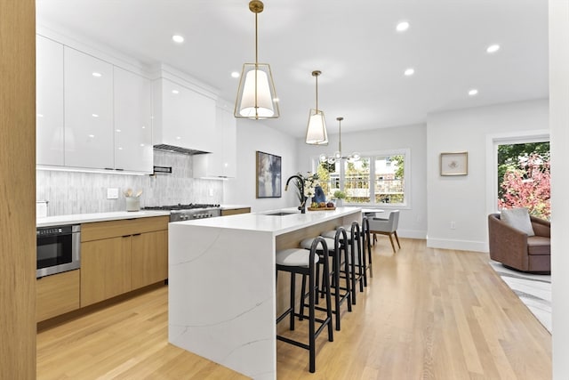 kitchen featuring light hardwood / wood-style floors, sink, an island with sink, white cabinets, and pendant lighting