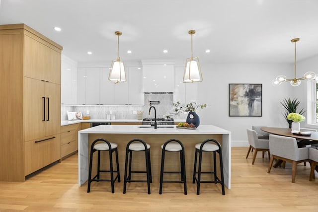 kitchen featuring white cabinetry, a center island with sink, sink, pendant lighting, and light wood-type flooring