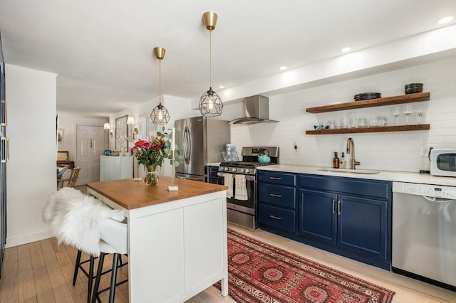 kitchen with blue cabinetry, a sink, appliances with stainless steel finishes, a breakfast bar area, and wall chimney exhaust hood