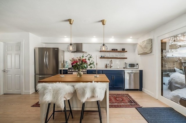 kitchen with light wood-style flooring, a sink, butcher block countertops, appliances with stainless steel finishes, and wall chimney exhaust hood