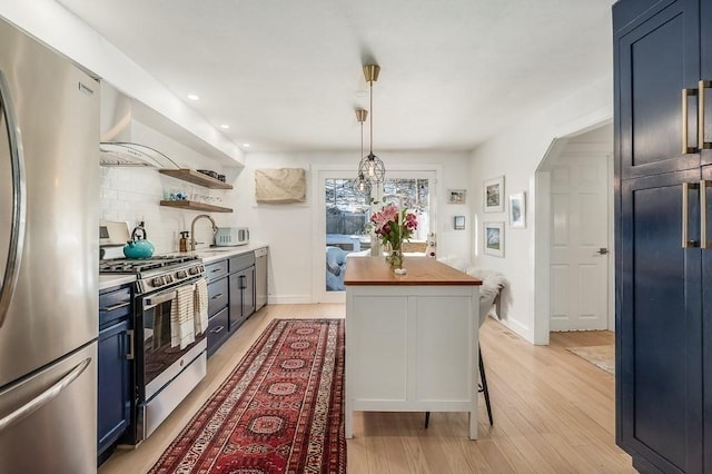 kitchen with open shelves, blue cabinetry, arched walkways, butcher block countertops, and appliances with stainless steel finishes