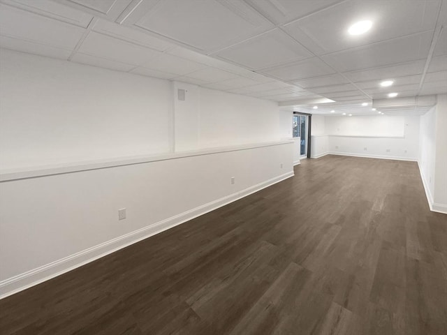 finished basement featuring a paneled ceiling, baseboards, and dark wood-type flooring