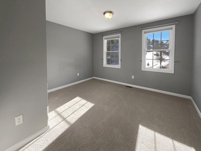 spare room with carpet floors, visible vents, and baseboards