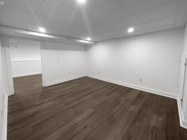 finished below grade area with dark wood-style flooring, a drop ceiling, and baseboards