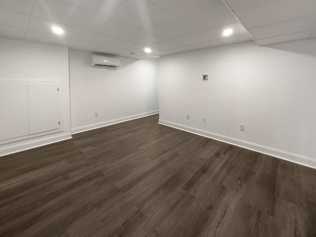 finished basement with a wall unit AC, dark wood finished floors, a drop ceiling, and baseboards