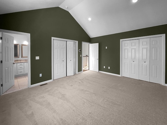 unfurnished bedroom featuring high vaulted ceiling, light colored carpet, visible vents, multiple closets, and ensuite bath