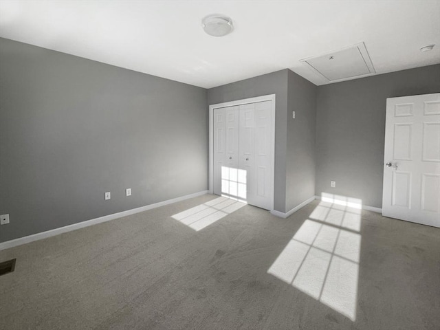 unfurnished bedroom featuring a closet, carpet flooring, attic access, and baseboards