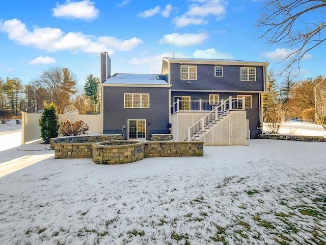 snow covered back of property with stairs, a chimney, fence, and a hot tub