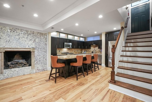 kitchen with light wood finished floors, stainless steel appliances, decorative backsplash, dark cabinetry, and a kitchen breakfast bar