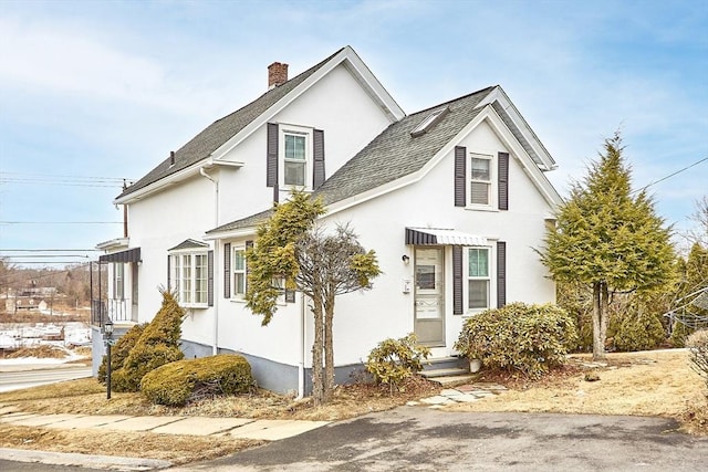 view of front of home featuring a shingled roof, a chimney, and stucco siding