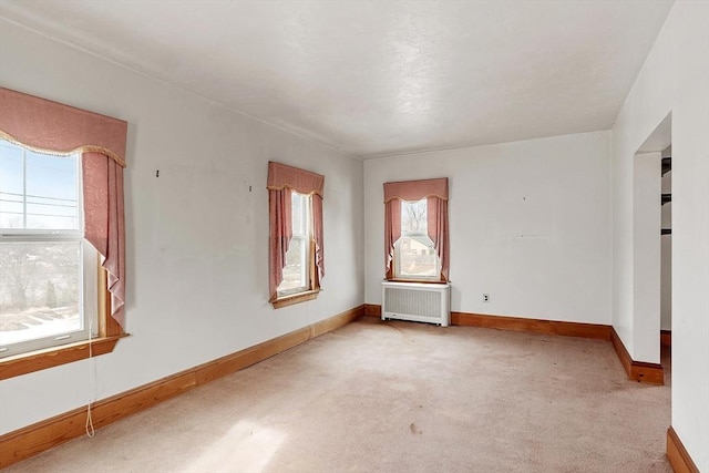 empty room featuring baseboards, light colored carpet, and radiator heating unit