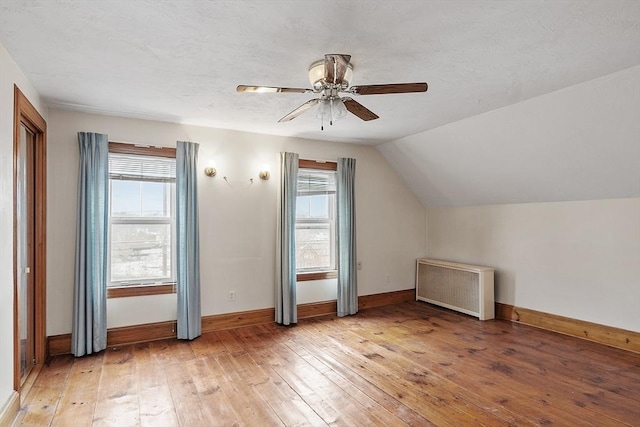 additional living space with radiator, a healthy amount of sunlight, light wood-style flooring, and lofted ceiling