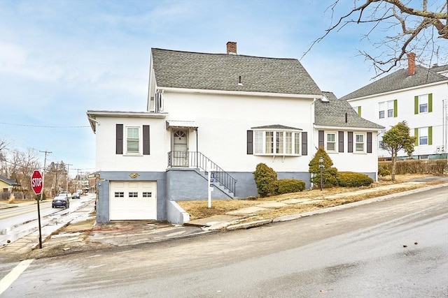 view of front facade with a shingled roof, a chimney, an attached garage, and stucco siding