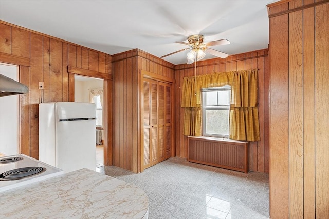 kitchen featuring radiator, brown cabinetry, freestanding refrigerator, a ceiling fan, and wooden walls