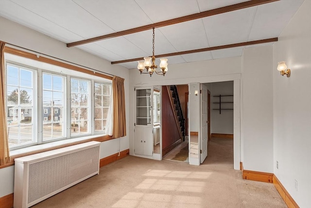 unfurnished dining area featuring radiator, light colored carpet, an inviting chandelier, beamed ceiling, and baseboards